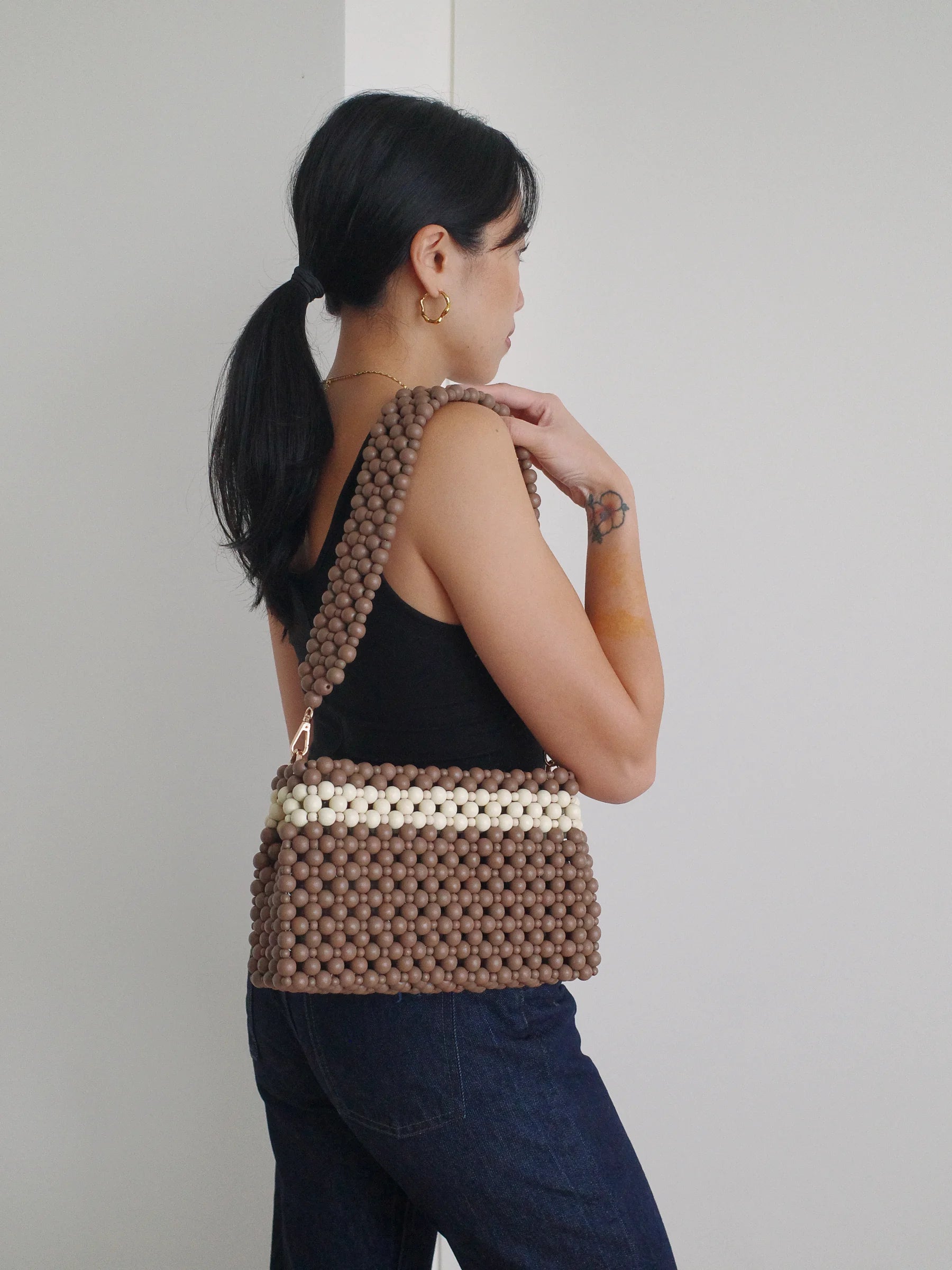 Woman carrying a brown beaded handbag against a plain background