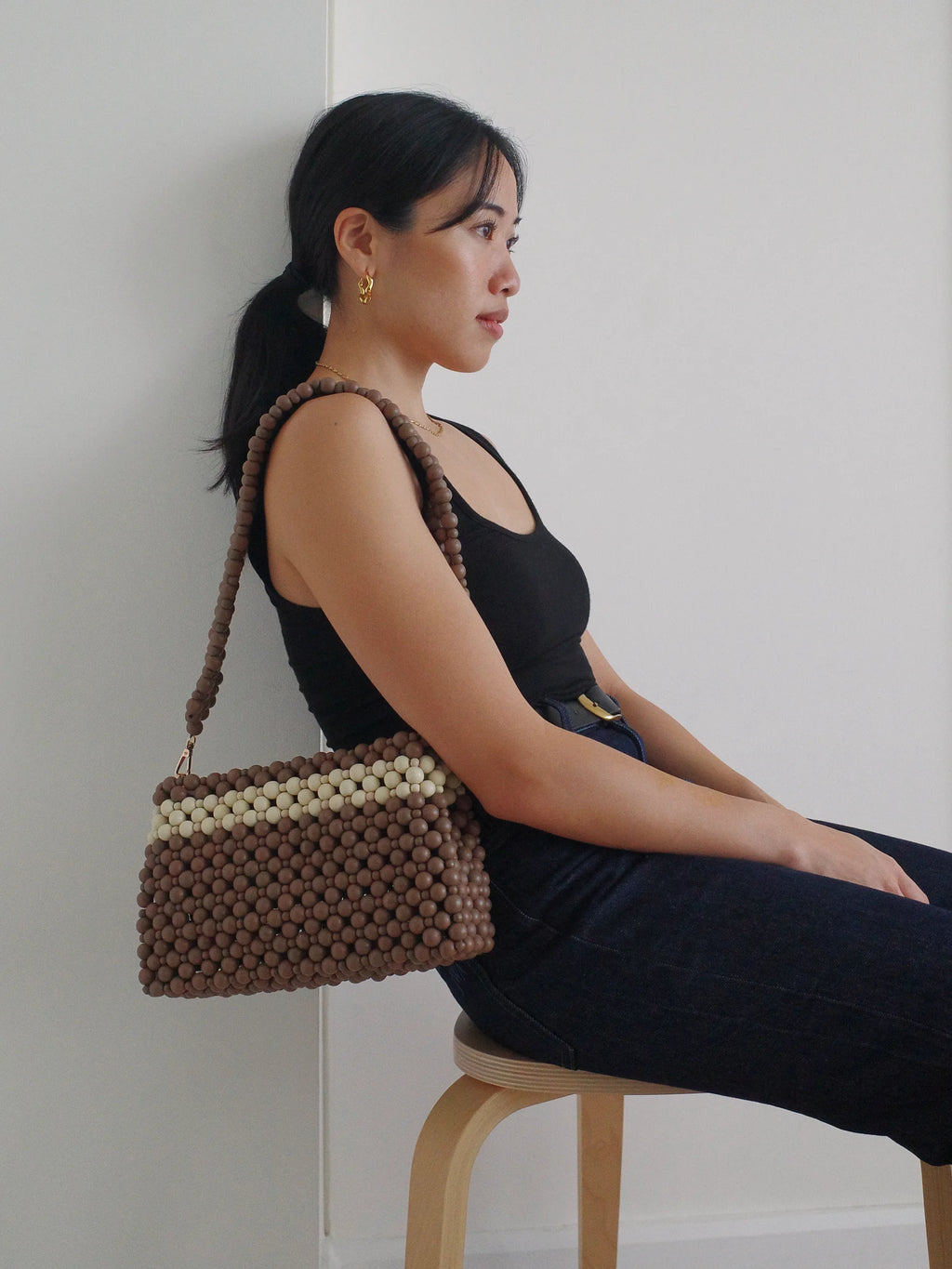 Woman holding a brown beaded handbag against a white wall