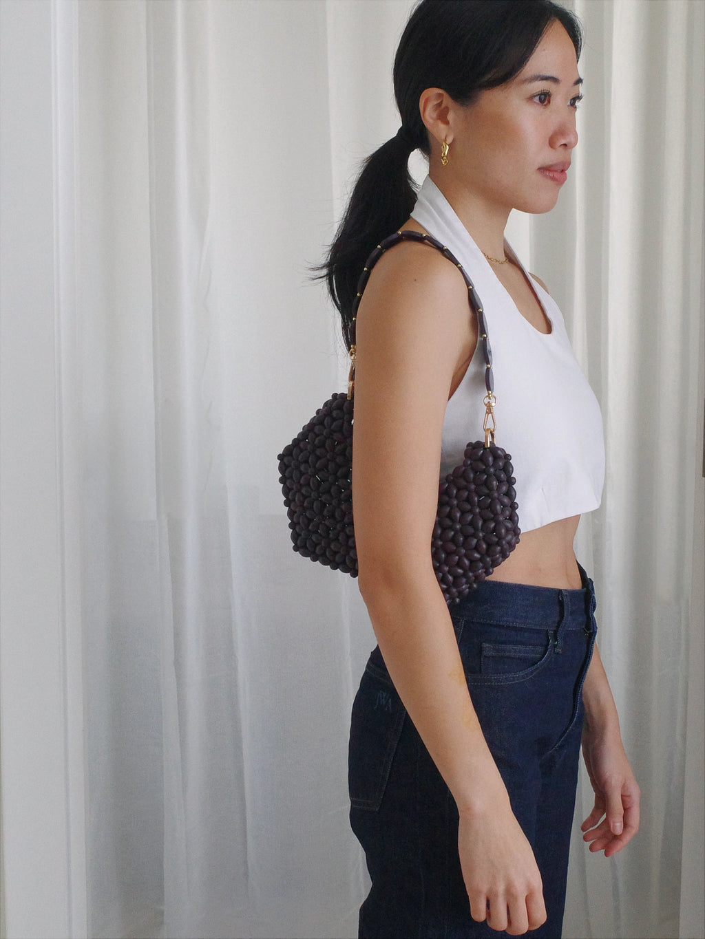 Woman holding a beaded handbag against a white curtain background