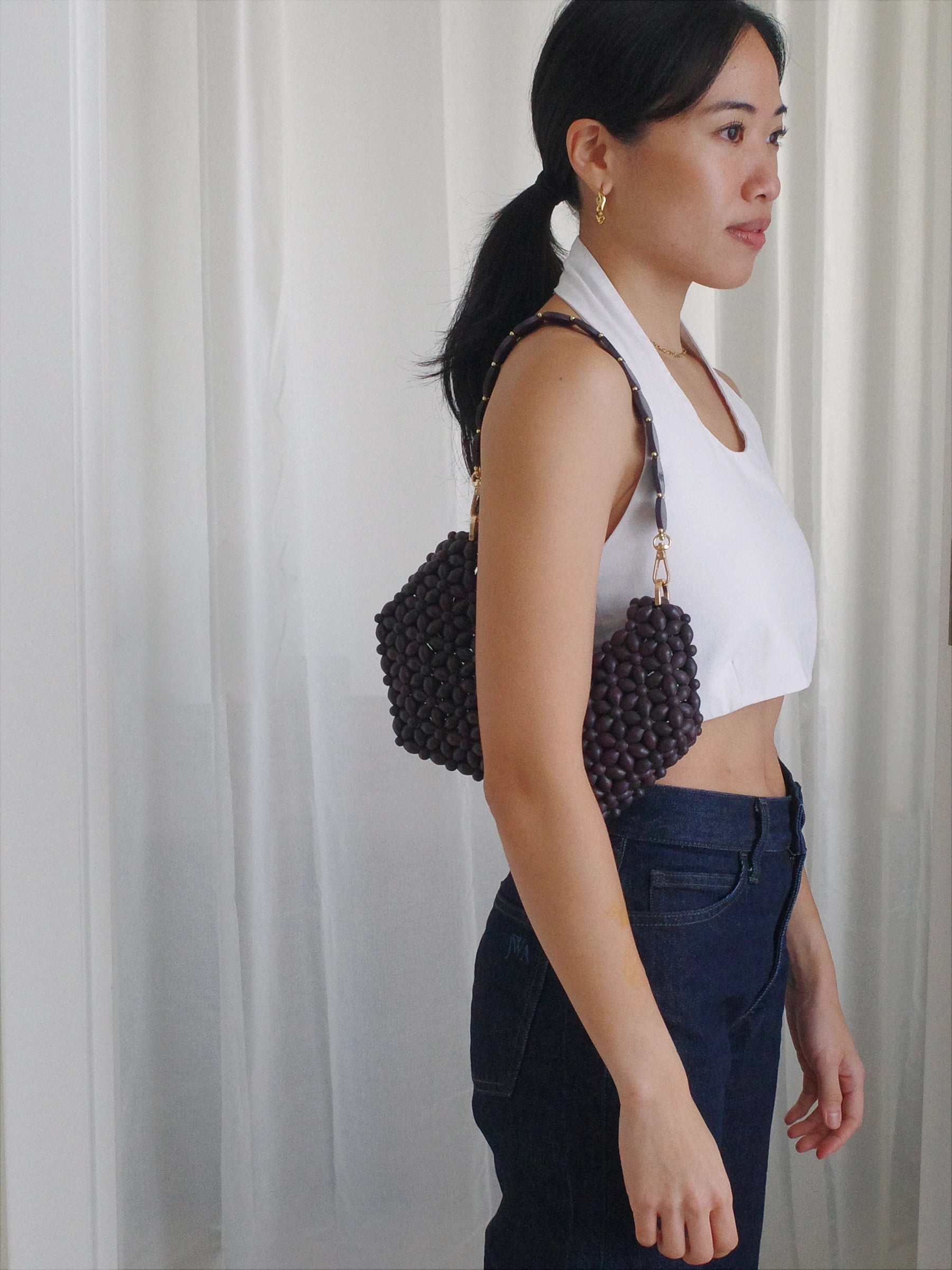 Woman holding a beaded handbag against a white curtain background
