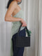 Person holding a black beaded handbag against a white curtain background